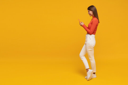 Side view of woman standing on yellow copy space background chatting online using phone