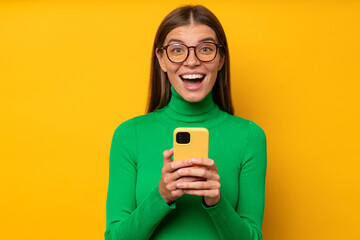 Lucky woman winner looking at camera with excited surprised face isolated on yellow background