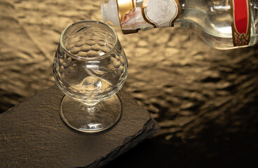 bottle of liquor, anis, tequila, rum, etc. glass on a slate stone and a water base with golden reflections. with space for text,