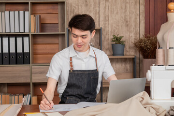 Asian young man fashion designer tailor working sketch the drawing clothes new collection in studio. Small business owner dressmaker making clothes in work shop, male entrepreneur working at home.