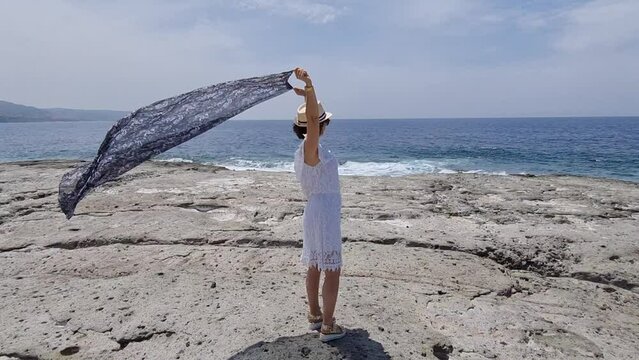 Rear view of a woman playing with the wind in pareo on Bosa Marina cliff in Sardinia on sunny day