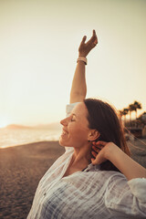 Cheerful young woman enjoying freedom on vacation on the seaside holding arms open on sunset