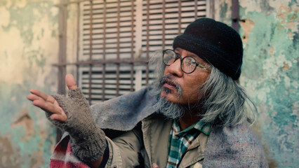 An old homeless Asian man is reaching out to a passerby asking for money for food because he has no...