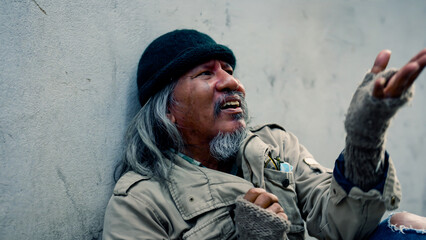 An old homeless Asian man is reaching out to a passerby asking for money for food because he has no job and no home and has to sleep on the streets at night. Homeless not have home