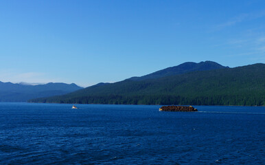 Tugboat towing barge with  fresh cut logs on Inner Passage, near Bella Bella, BC, with mountain backdrop
.