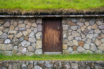 Ein Haus aus Feldsteinen mit einer Holztür und Grasdach, Färöer Inseln