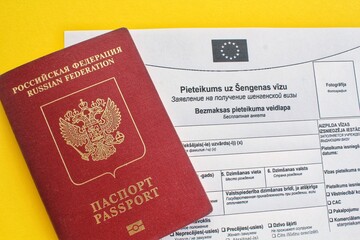 Schengen visa application form in Russian and Latvian language and passport on yellow background. Prohibition and suspension of visas for tourists to travel to European Union and Baltic States concept