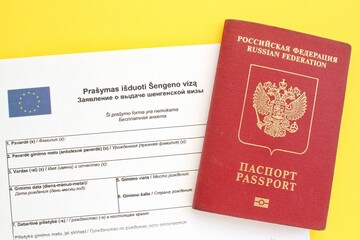 Schengen visa application form in Russian and Lithuanian language and passport on yellow background. Prohibition and suspension of visas for tourists travel to European Union and Baltic States concept