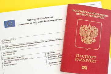 Schengen visa application form in Russian and Estonian language and passport on yellow background. Prohibition and suspension of visa for Russian tourists to travel to European Union and Baltic States