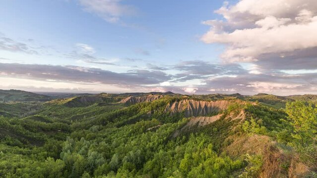 Sunset over Italian badlands and green hills with colored clouds in the sky, Italy