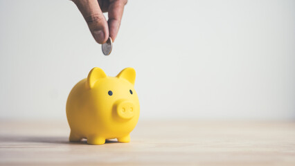 Hand of people putting coins in piggy bank on wooden table. Concept saving money finance business investment.