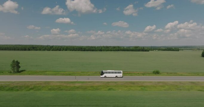 Travel tour bus driving alone on straight highway through plain field. White bus fast speed moving on freeway. Aerial drone wide shot at summer sunny day.