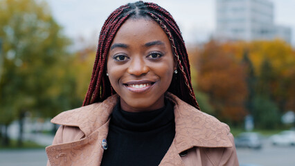 Female portrait close-up young satisfied happy african american woman standing in autumn park looking at camera smiling with white teeth attractive joyful girl model with stylish hair posing outdoors