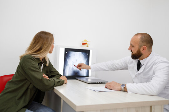 Male orthopedist doctor showing x-ray to female patient at medical office