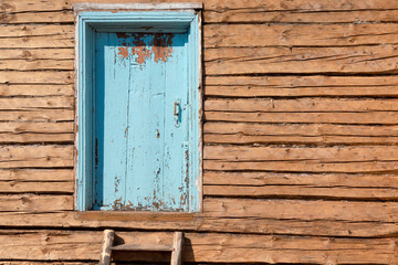 Wall of an old village house made of logs during renovation. There is an old door with peeling blue paint and a small ladder. Background. Concept.