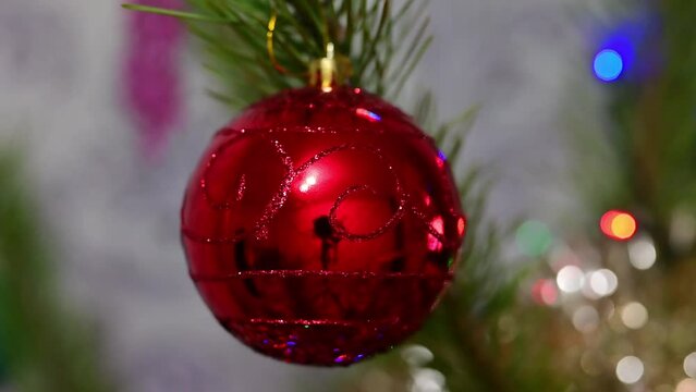 Christmas tree decorated with red glass ball on christmas spruce branch on background bokeh of flickering light bulbs garlands. Happy New Year festival mood. Positive emotion.