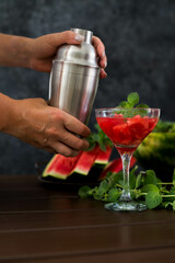 watermelon alcoholik or non- alcoholic cocktail with mint and woman hand with shaker on dark background