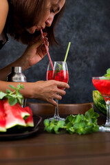 Cute woman is drinking watermelon cocktail on dark background.