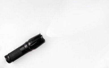 A black metal flashlight shines on a white background. Copy space. Concept