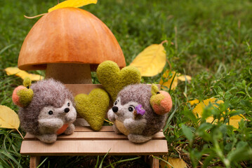 Date under a mushroom made of pumpkin and salt dough, on a plywood bench near two felted hedgehogs in the afternoon, surrounded by green grass, felted hearts and yellow leaves