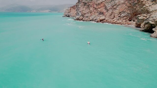Aerial circular view of family rowing on stand up paddle boards. Mom and dad oaring on paddleboards with their sons down azure sea