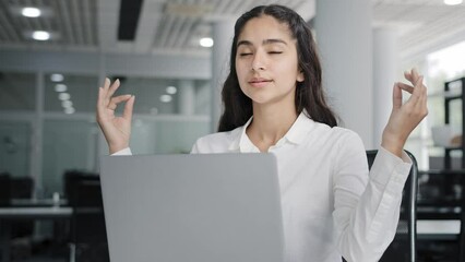 Young balanced girl manager sitting in office near laptop taking break meditates relaxes does breathing practice relaxed woman reducing stress during workday meditating in workplace feeling relieved