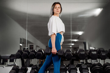 Fototapeta na wymiar Sporty fitness girl doing exercises using a dumbbells in the gym