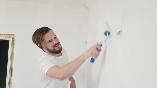 close-up of a young man with a funny mustache curled up very diligently paints the wall with a roller with white paint. the concept of home renovation, renovation in the apartment