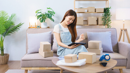 Obraz na płótnie Canvas Online shopping concept, Female entrepreneur checks online orders on tablet to prepare parcel boxes