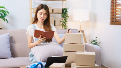 Obraz na płótnie Canvas Online shopping concept, Female entrepreneur writes on parcel box after reading address on notebook