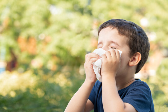 Allergic child sneezing covering nose with wipe in a park in spring or summer season