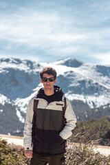 Handsome caucasian man posing to camera. He carries his cell phone and sunglasses. he has snowy mountains in the background