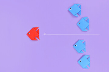 Red origami paper fish swimming ahead of line of blue fish. Concept for new business strategies,...
