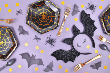 Halloween party flat lay with spider web plates, costume bat headband, spiders and confetti on...