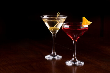 two cocktail glasses with martini, olive and orange on rubber stand on pub bar seen from the front landscape format