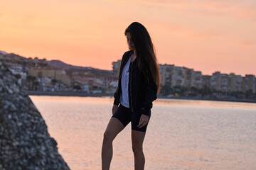 Fototapeta na wymiar young hispanic girl posing at the rocks of a beach in the mediterranean sea while sunrise