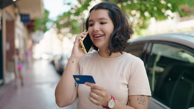 Young woman talking on the smartphone and using credit card at street