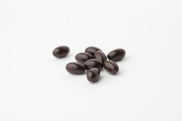 Black soft gel capsules in blue spoon on white background. Vitamin E dietary supplement. Closeup