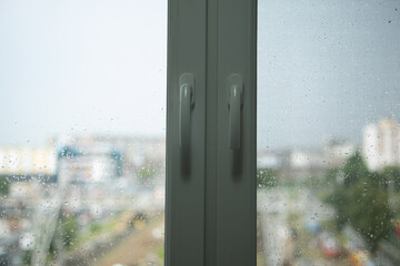 Plastic window frame with fittings. Raindrops on the window. In the background is a blurred image of the city