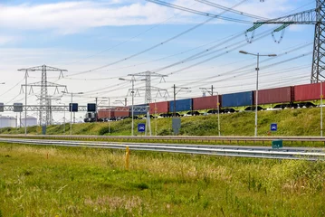 Zelfklevend Fotobehang Cargo train carrying containers along a motorway in a port area on a clear summer day © alpegor