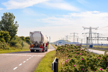 Tanker truck on a narrow road running along a motorway and railway in a port area with electricity...