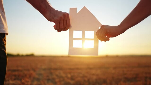 paper house happy family. friendly family hands holding paper house the glare of the sun shine through the window a beautiful sunset. mortgage lifestyle business construction concept. house dreams