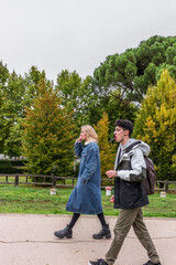 two handsome friends, a man and a woman walking in a green park. Its Autumn