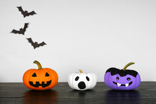 Painted Halloween pumpkins on a black wood shelf against a white background with bats. Jack o Lantern, ghost and vampire.