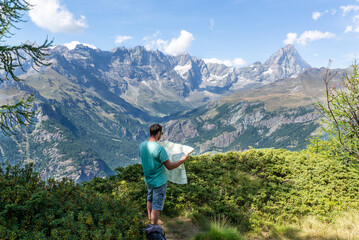 Standing man looking a map during a hiking day at Aosta Valley in italian alps. Active vacations around Matterhorn. 