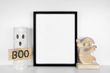 Halloween mock up. Black frame on a white shelf with rustic wood ghost decor. Portrait frame...