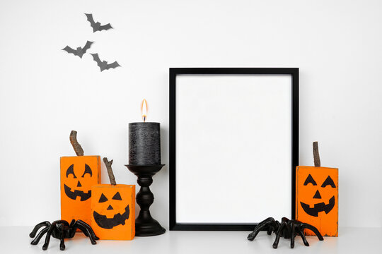 Halloween mock up. Black frame on a wood shelf with rustic wood jack o lantern decor, spiders and candle. Portrait frame against a white wall with bats. Copy space.