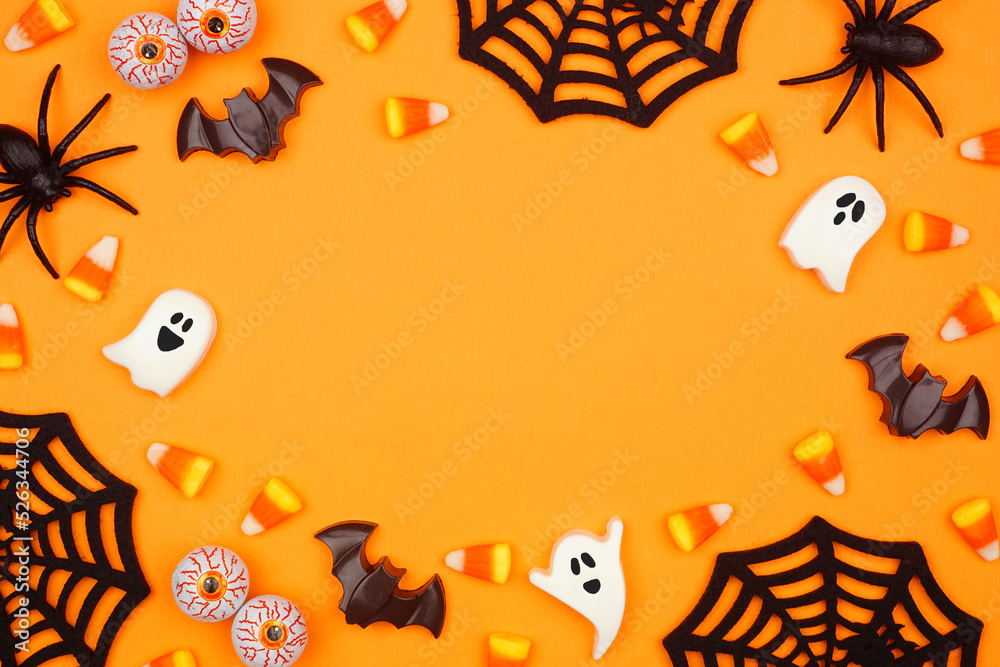 Poster Halloween frame of scattered candy and decor. Top down view over an orange background with copy space.