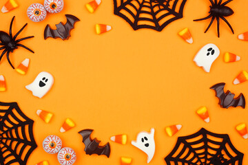 Halloween frame of scattered candy and decor. Top down view over an orange background with copy...