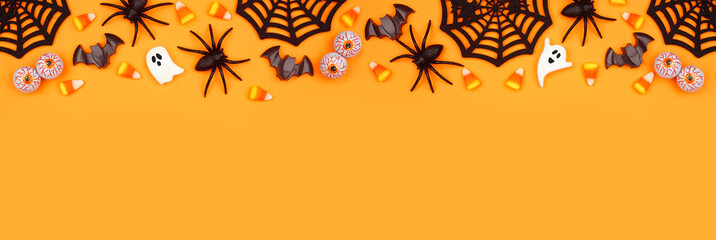 Halloween top border of scattered candy and decor. Above view over an orange banner background with copy space. - obrazy, fototapety, plakaty